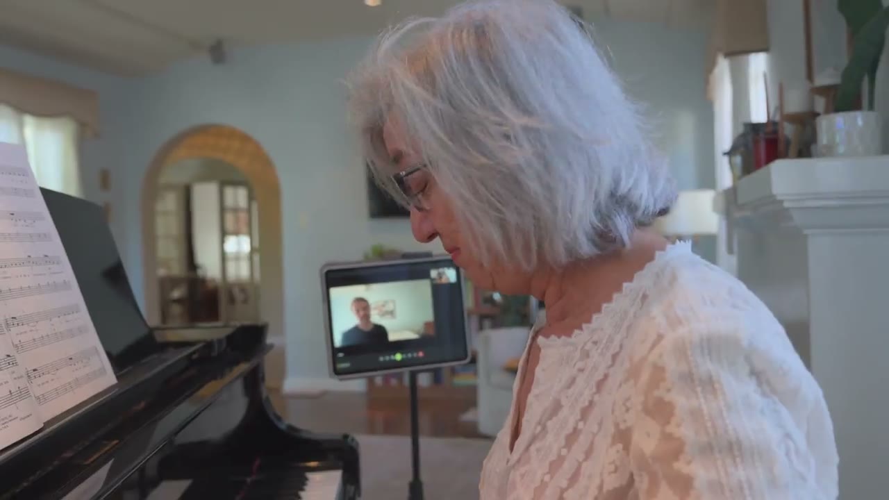 A student at the piano during a live lesson, with the teacher on the screen beside them